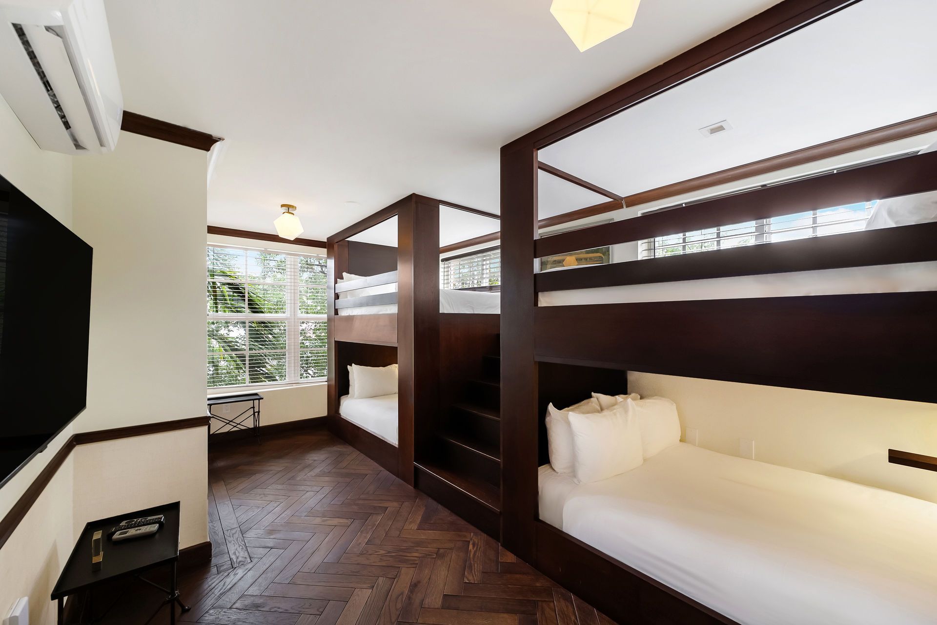 Bunk beds in a room. Dark wood frames, white bedding, large window, and a mounted TV.