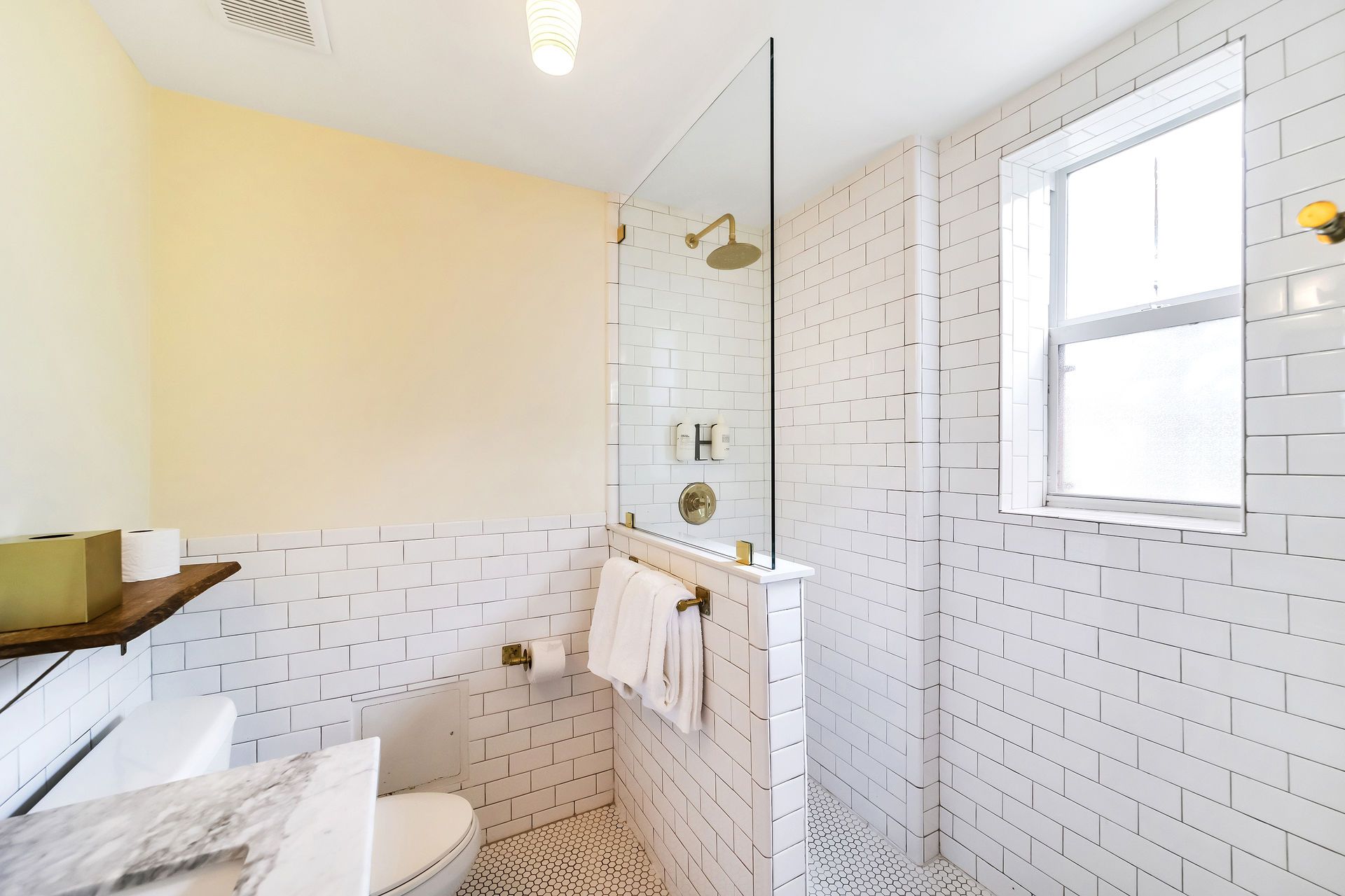 Bathroom with white subway tiles, glass shower, gold fixtures, and a window.
