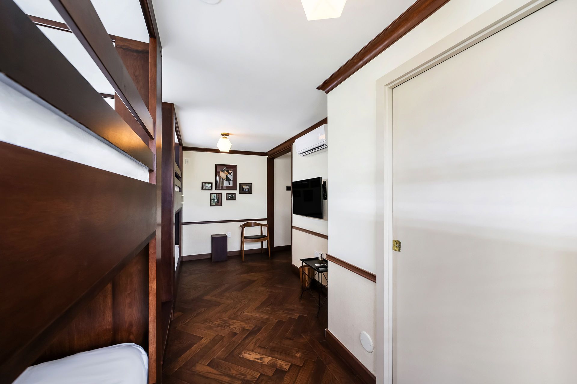 Hallway with dark wood paneling, parquet floor, bunk bed, and closed white door.