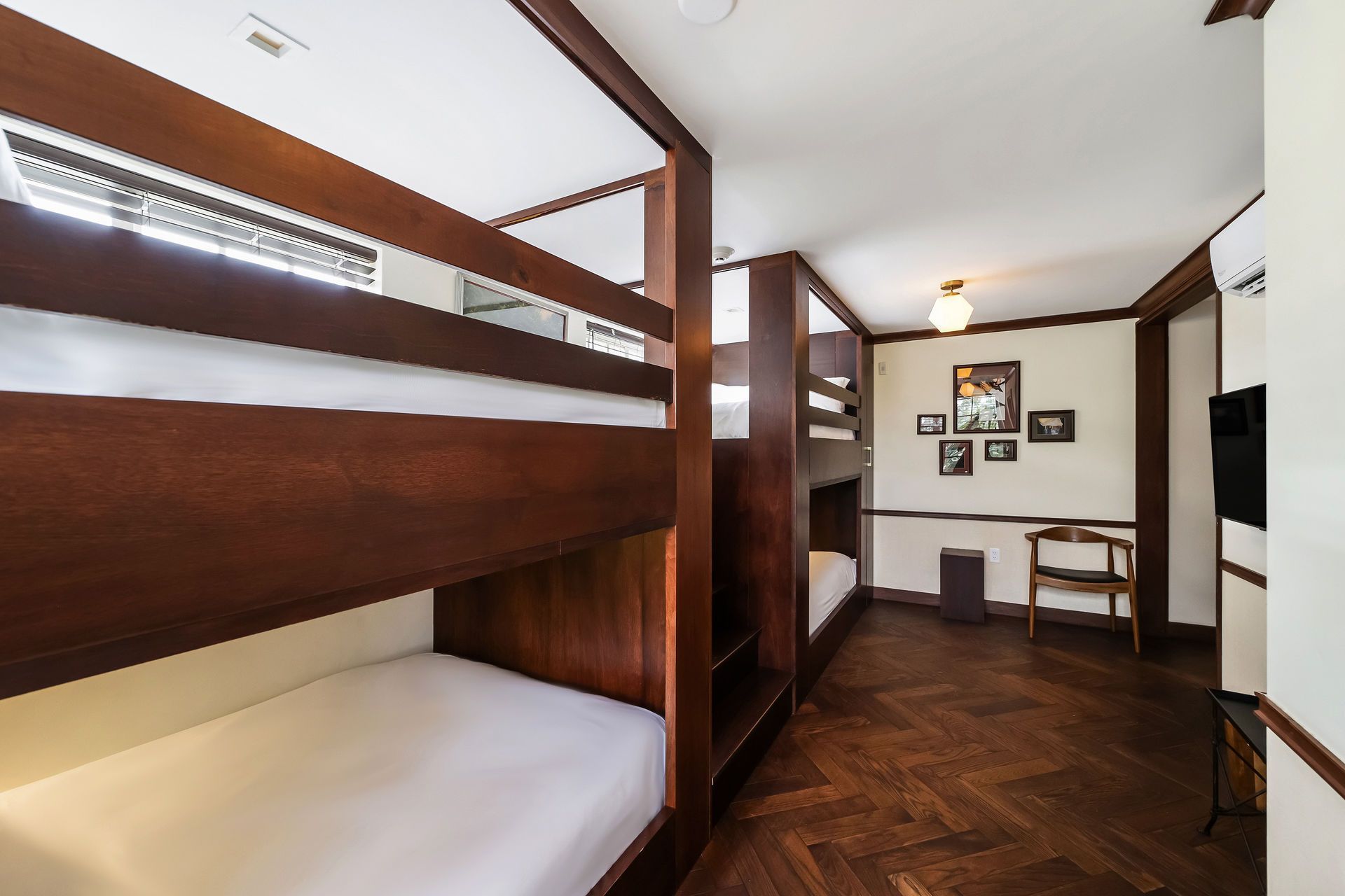 Room with multiple wooden bunk beds, hardwood floors, and framed art.