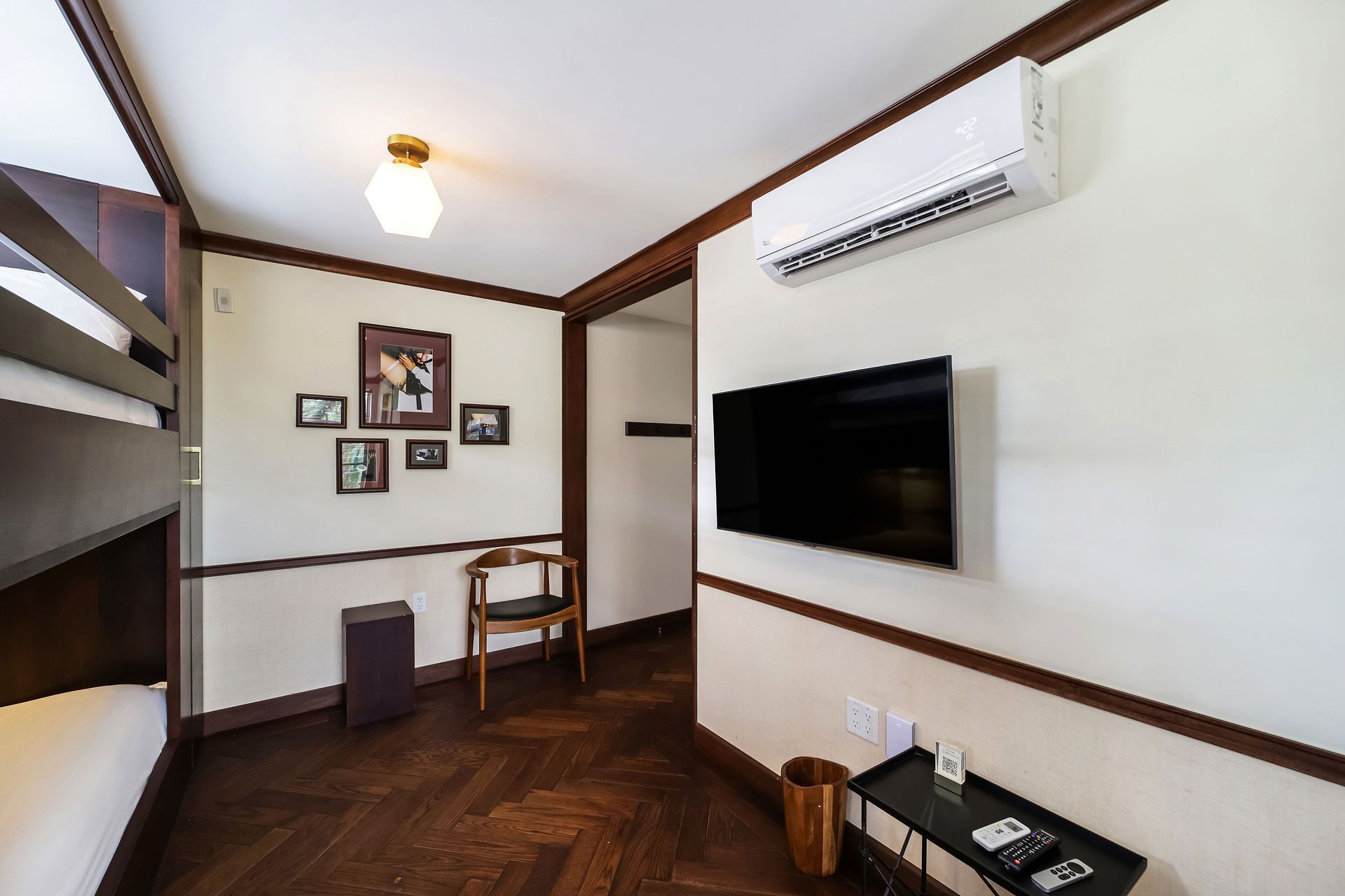 Bedroom with bunk beds, TV, air conditioner, and wooden accents; dark wood flooring.