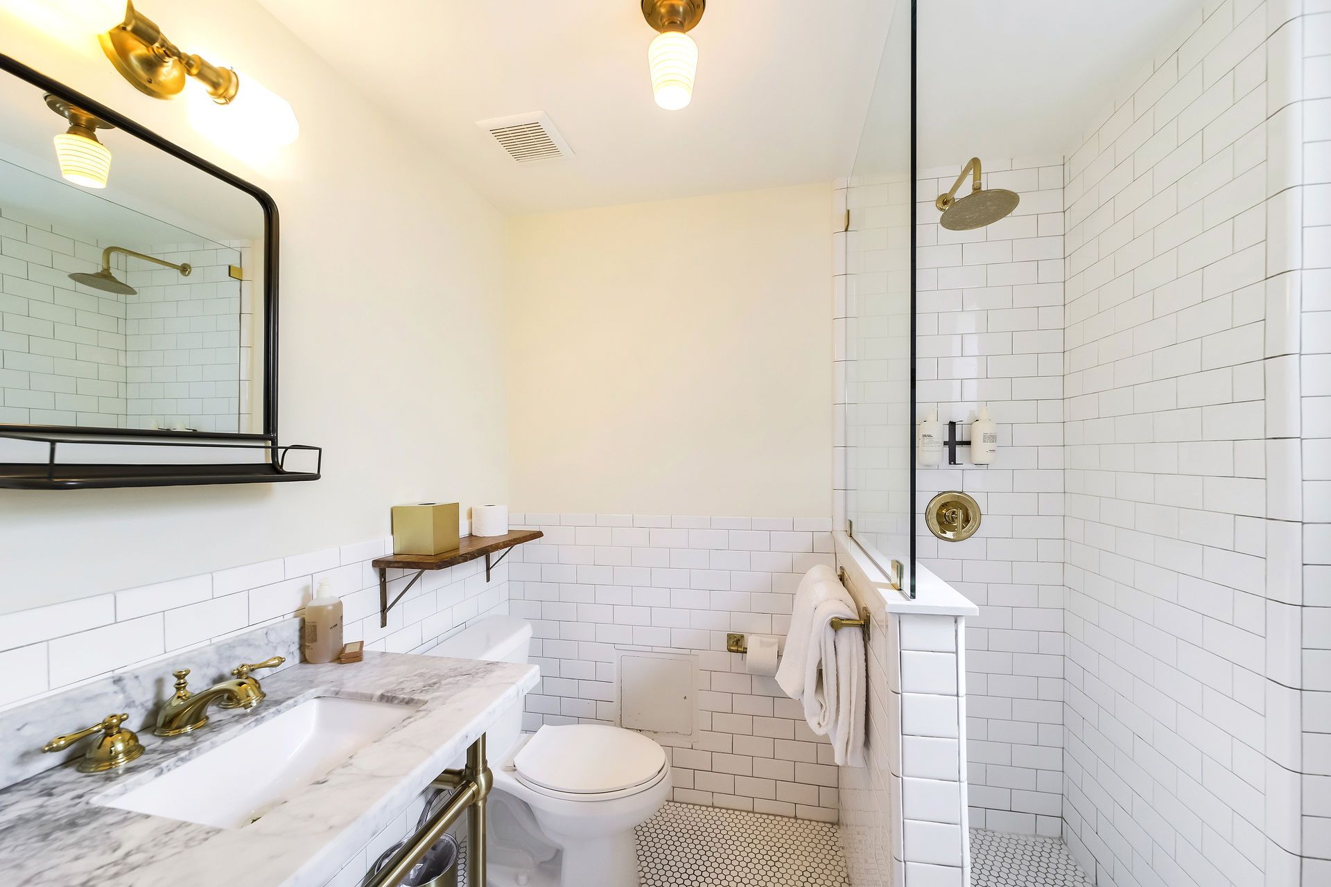 Bathroom with white subway tiles, marble countertop, brass fixtures, and glass shower.