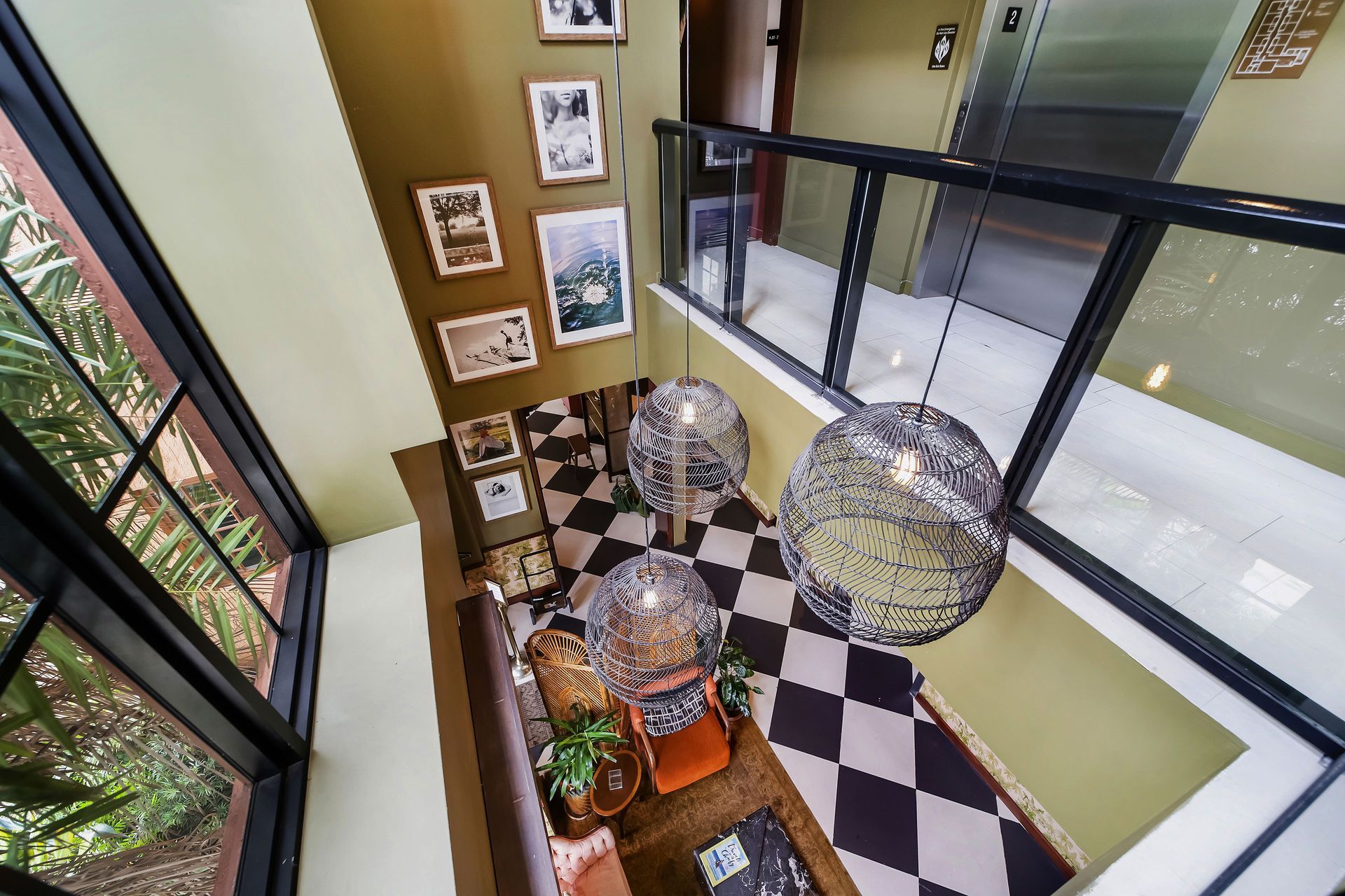 A high-angle view of a lobby with a black and white checkered floor, brown couch, and hanging pendant lights.