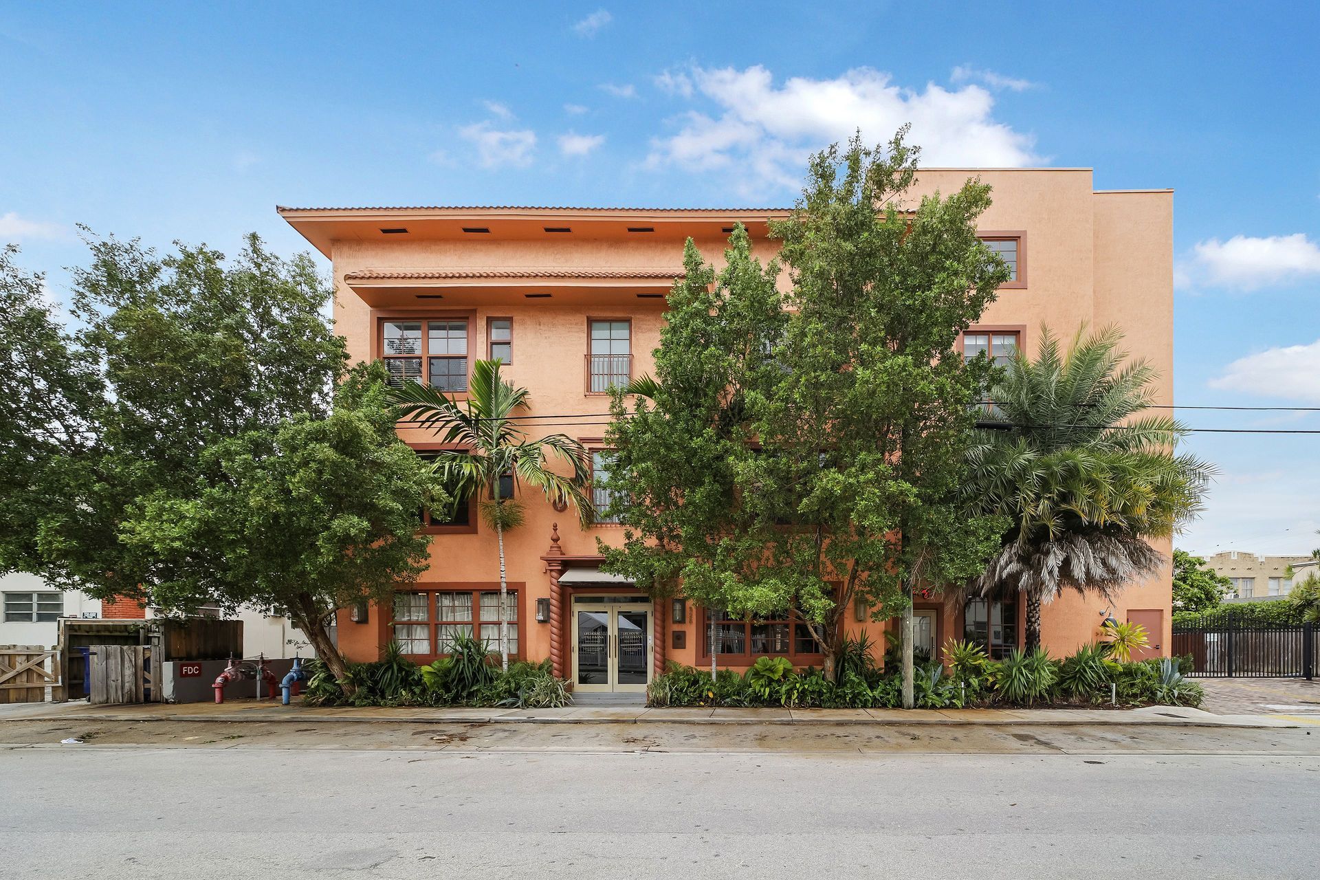 Three-story peach-colored apartment building with trees in front; blue sky overhead.