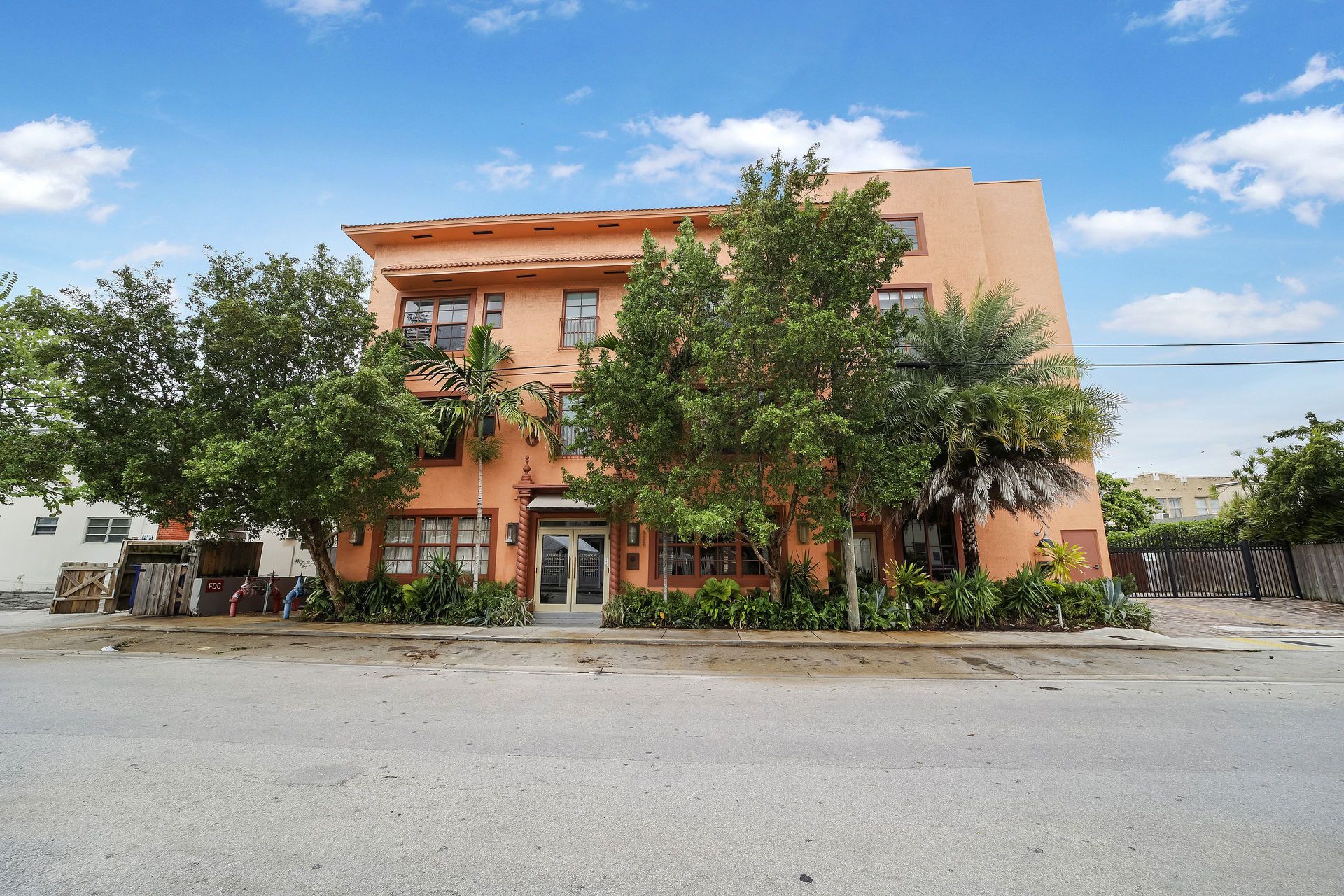 An orange stucco building with a flat roof, trees in front, and a blue sky.