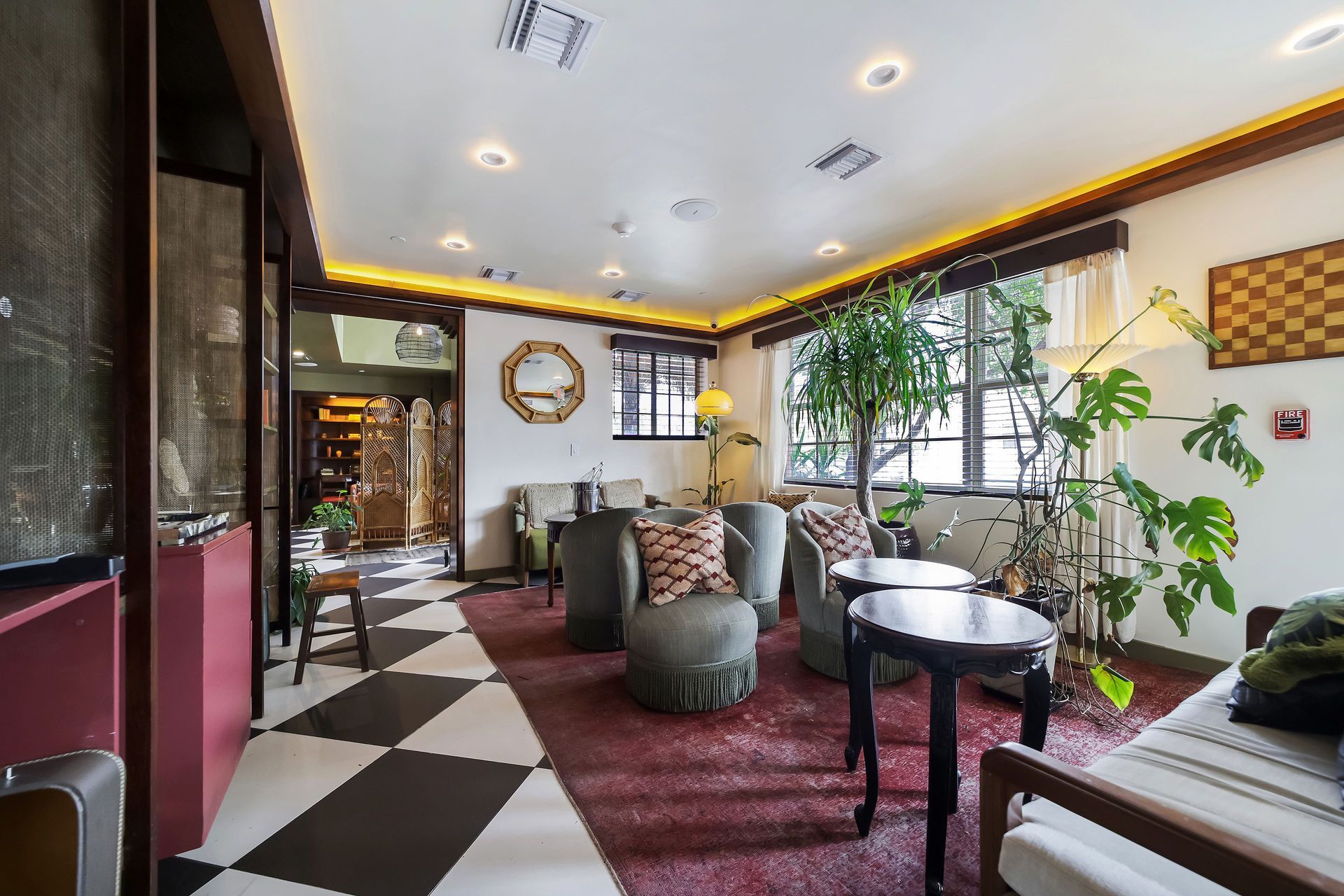 Cozy lounge area with checkerboard floor, velvet seating, plants, and vintage decor.