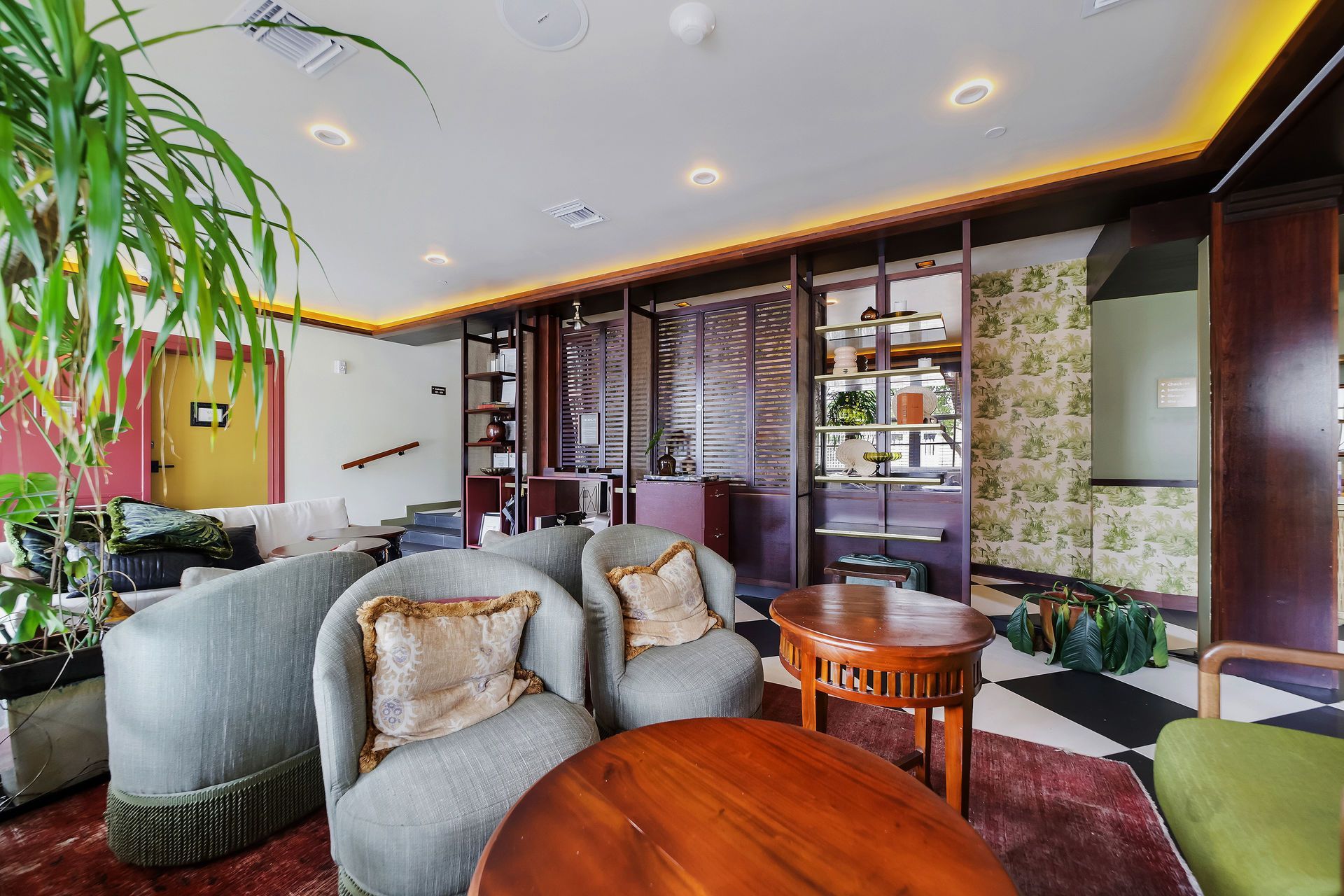 Lounge area with gray seating, wooden tables, bookshelves, patterned wallpaper, and potted plants.