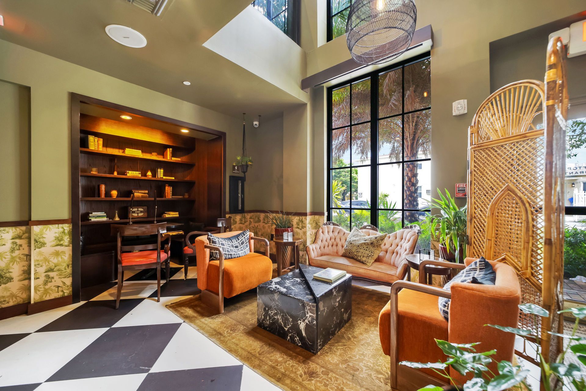 Cozy lounge with orange seating, patterned rug, checkered floor, large window, and built-in shelves with décor.