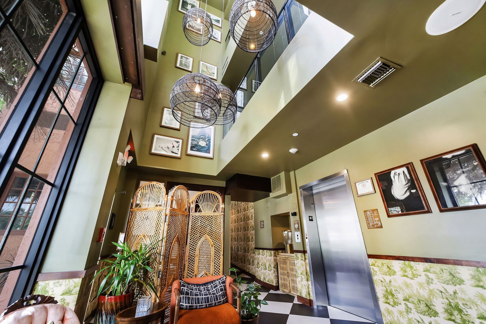 Lobby with decorative hanging lights, an elevator, patterned screen and walls, framed art, and seating area.