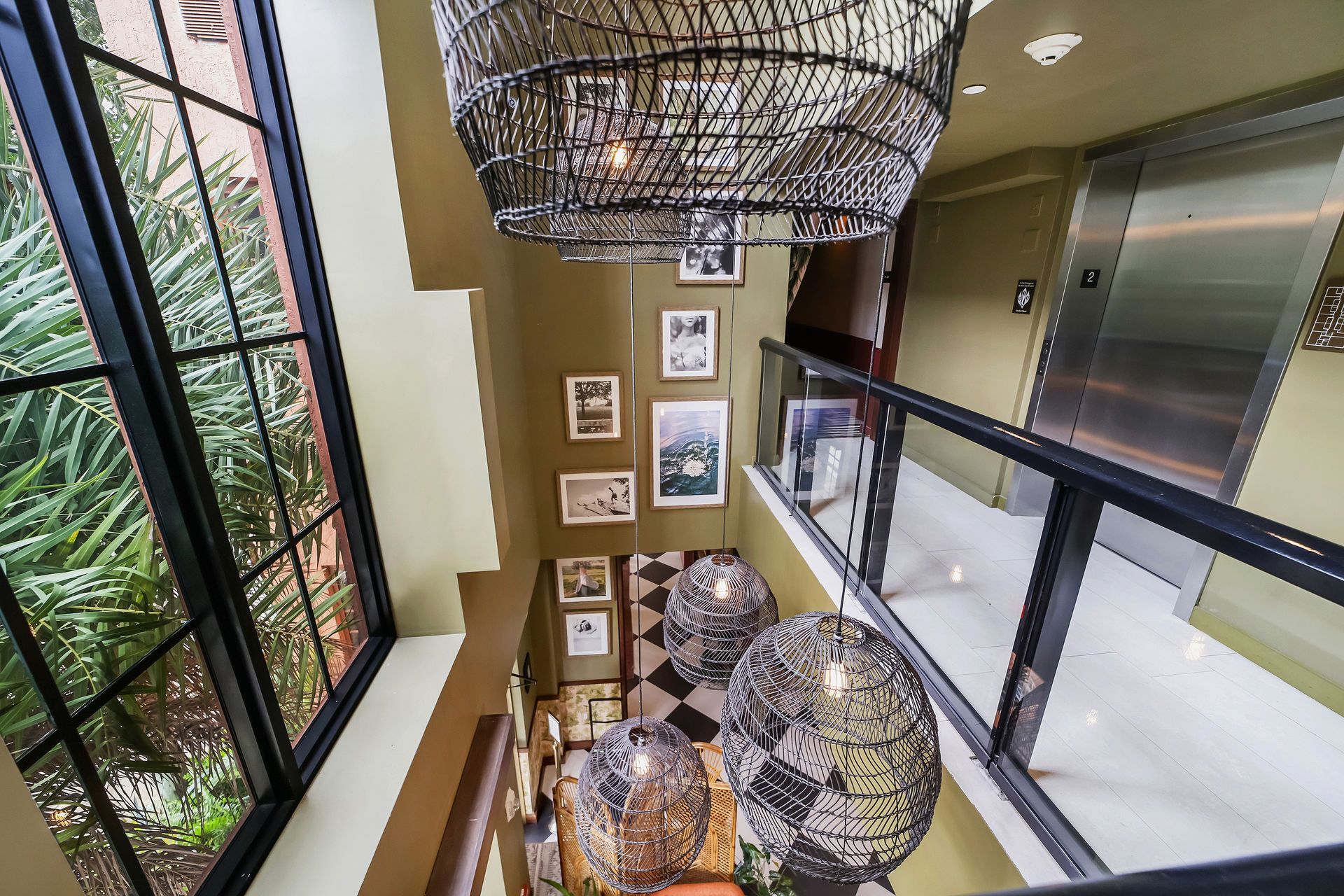Stairwell with decorative pendant lights, framed artwork on the wall, and elevator. Black and white tiled floor.