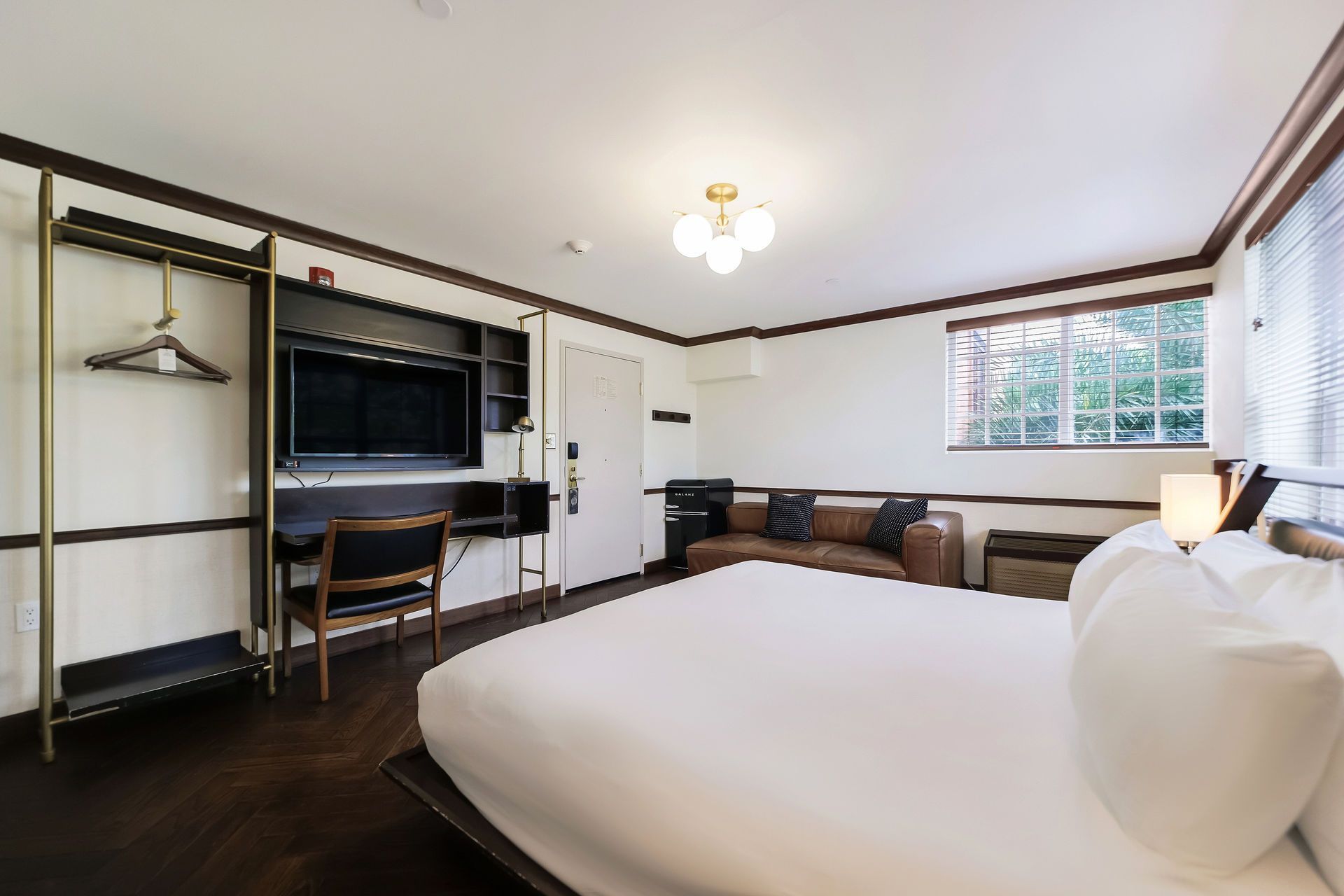 Hotel room with a bed, desk, television, and a brown leather couch near a window.