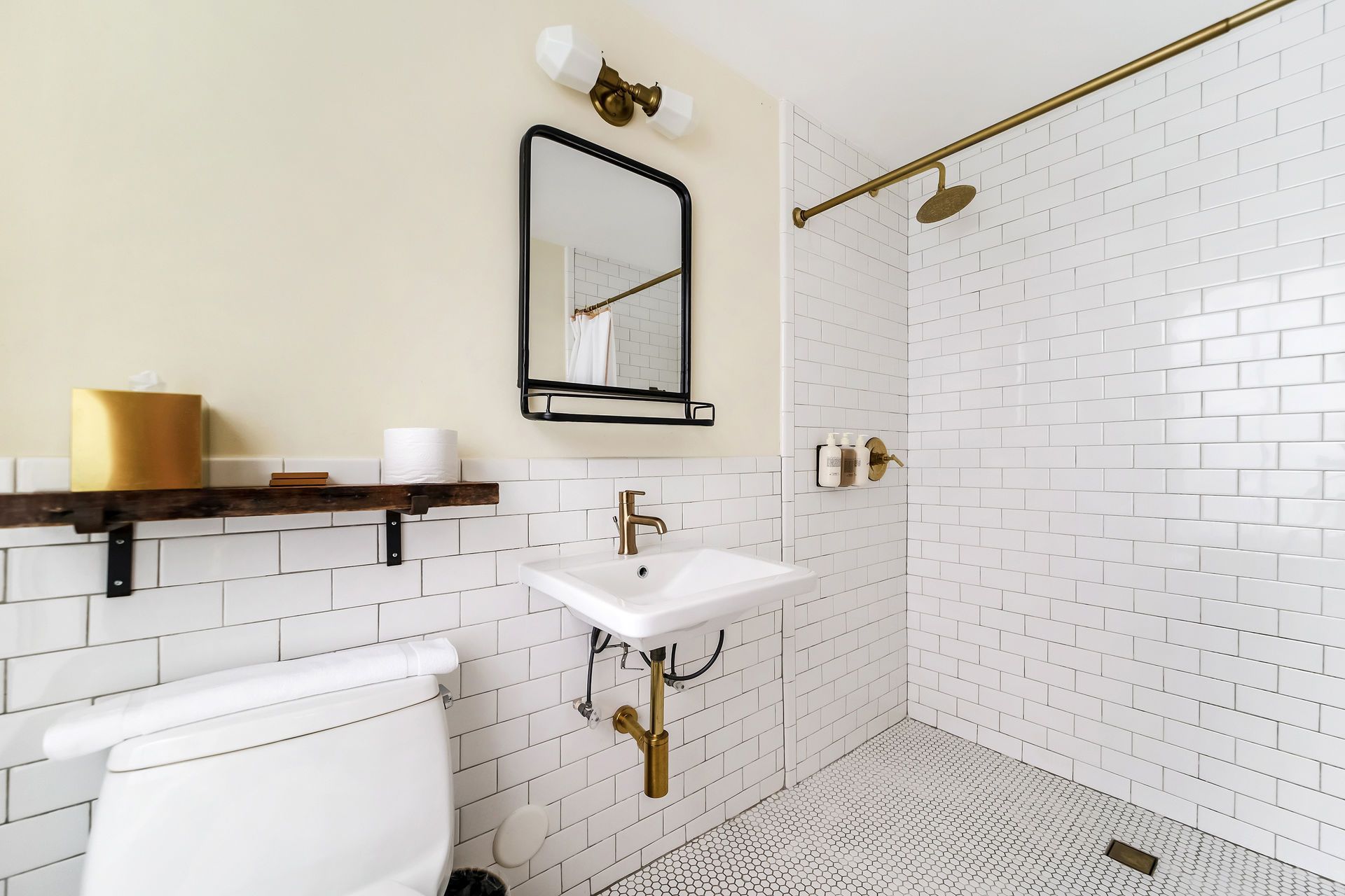 Bathroom with white brick tile, gold fixtures, and a black-framed mirror.