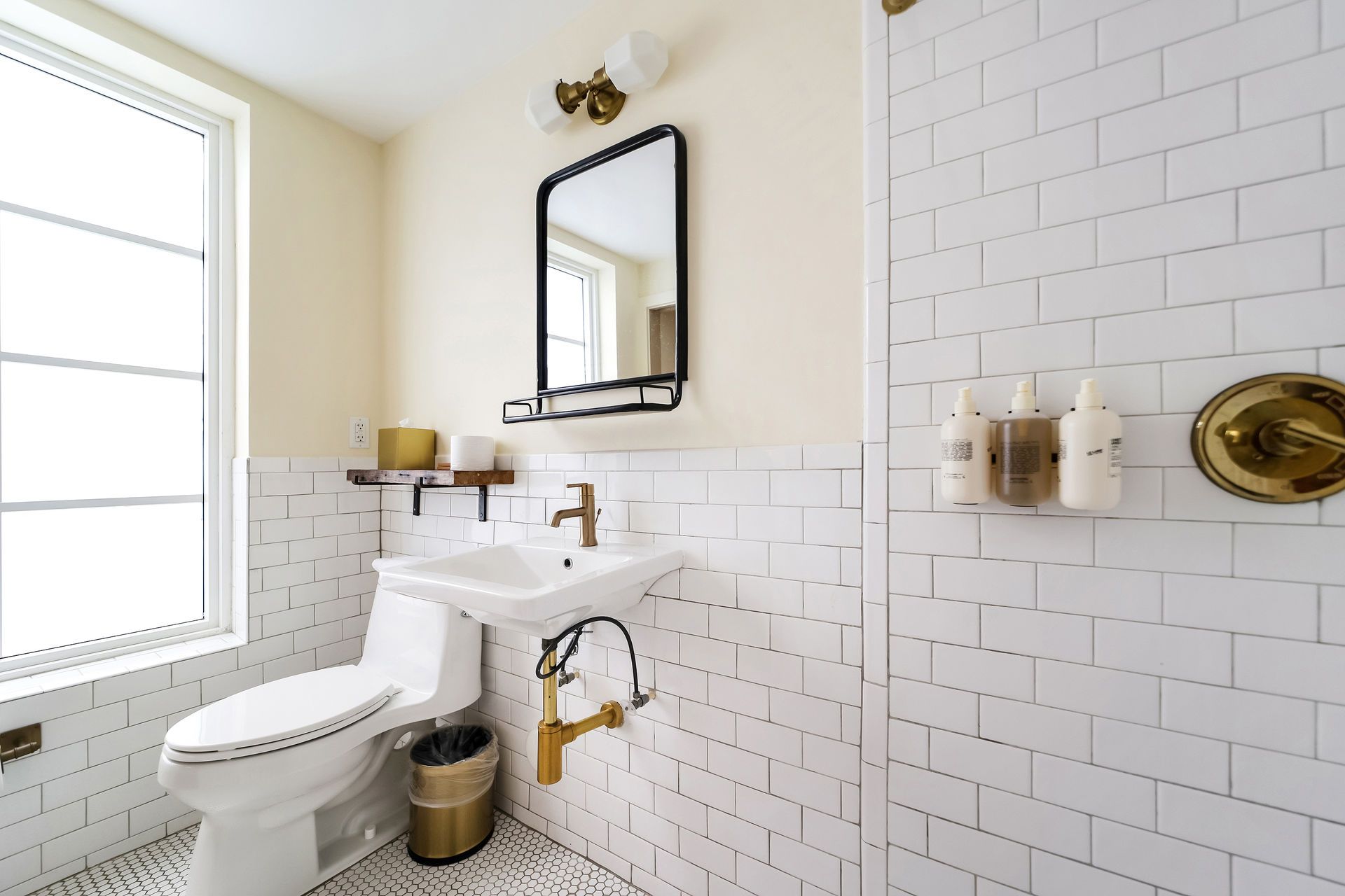 Bathroom with white subway tile, a toilet, sink, mirror, and shower. Gold fixtures.