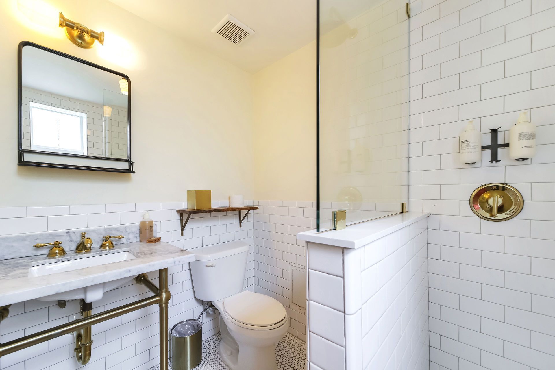 Bathroom with white subway tiles, glass shower, gold fixtures, and a marble sink.