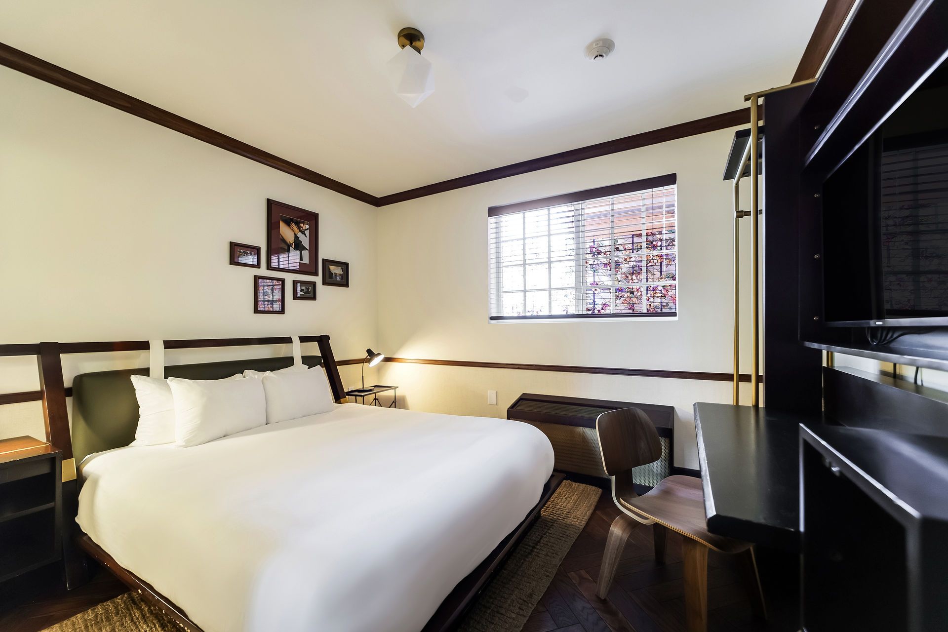 Bedroom with bed, desk, and window. White bedding, dark wood trim, and a brick exterior visible.