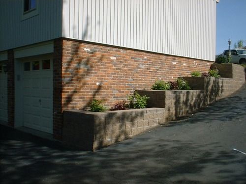 Brick and siding building with tiered retaining wall planters and asphalt driveway.