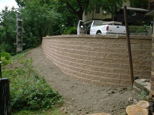 Beige brick retaining wall on a hillside with a white truck parked above it.