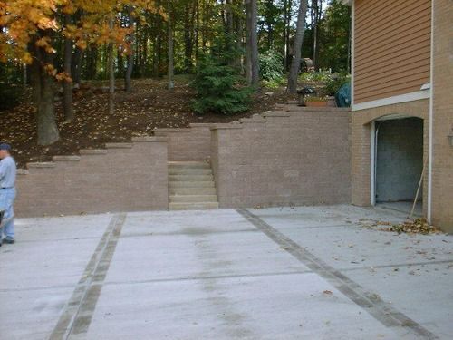 Concrete driveway with retaining wall, stairs, and garage. Man stands near the driveway.