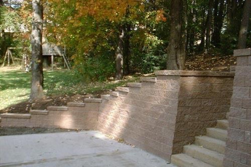Brick retaining wall with built-in steps on a sloping yard with trees.