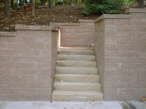 Concrete stairs between tan retaining walls lead up to a forested area.