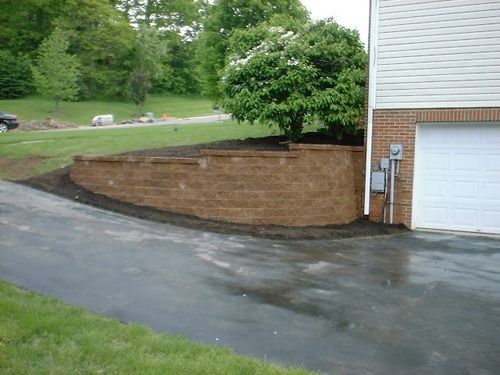 A retaining wall with landscaping next to a building and driveway.