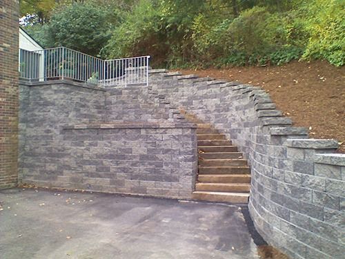 Stone retaining walls with stairs leading up to a platform with a railing, set into a hillside.