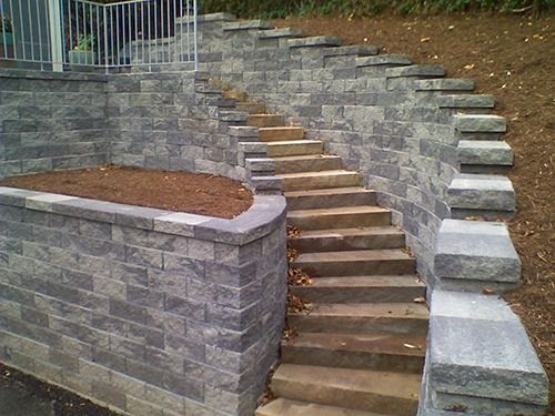 Stone staircase built into a retaining wall, leading upwards; grey blocks, brown dirt on left.