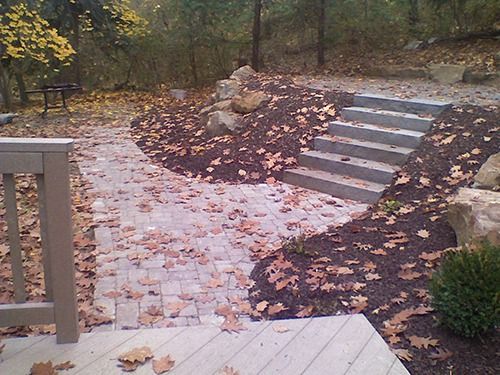 Stone path and stairs leading to a wooded area, covered in fallen leaves.