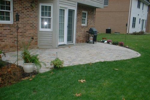 Brick house with stone patio and grill, surrounded by green grass.
