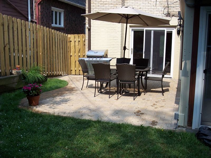 Backyard patio with table, chairs, grill, and umbrella, adjacent to grass, fence, and house.