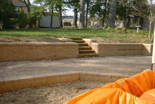Brick retaining walls and steps in a yard, leading up to a grassy area.