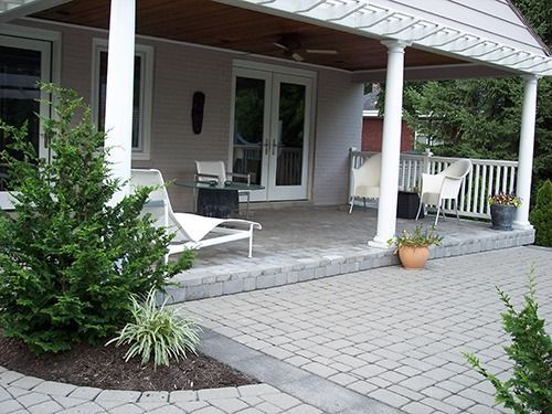 Patio with pavers and white columns, furnished with chairs, under a pergola-style roof.