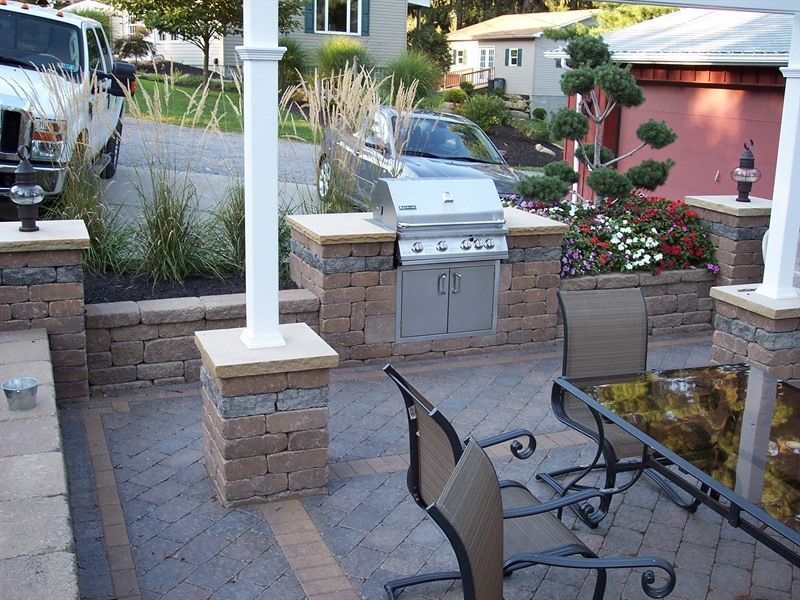 Outdoor kitchen with built-in grill, brick columns, and dining set on a brick patio.