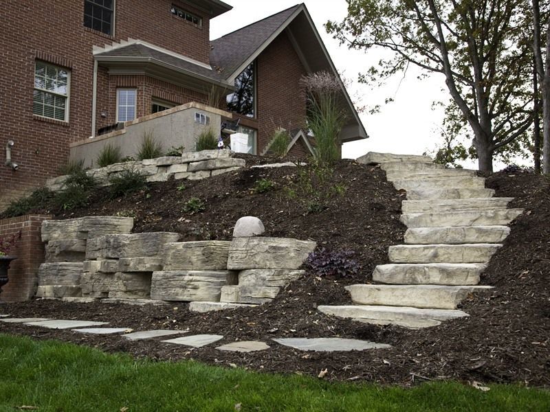 Stone steps and retaining wall leading up a sloped yard next to a brick building.
