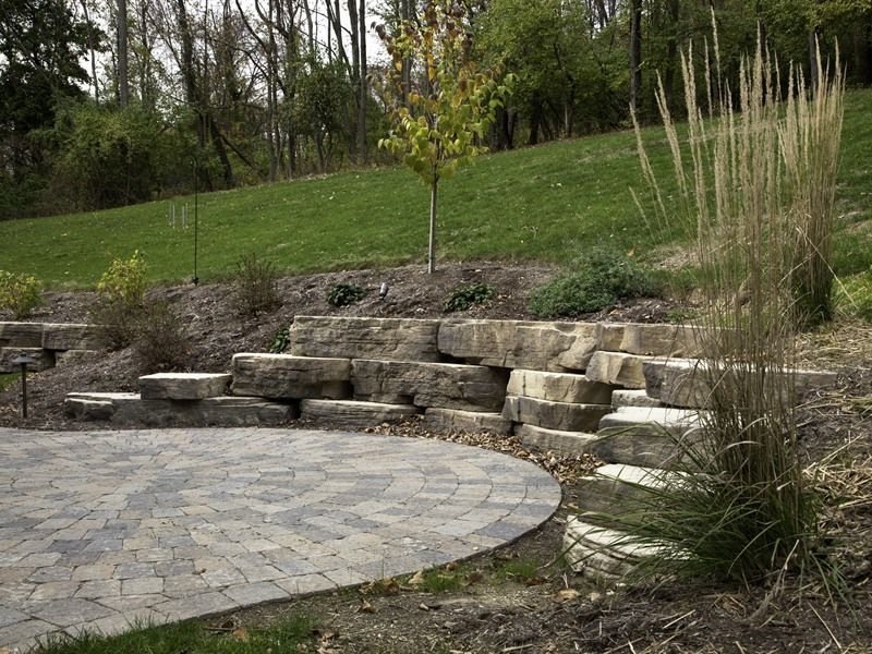 Stone retaining wall and paved patio with grassy hillside in the background.