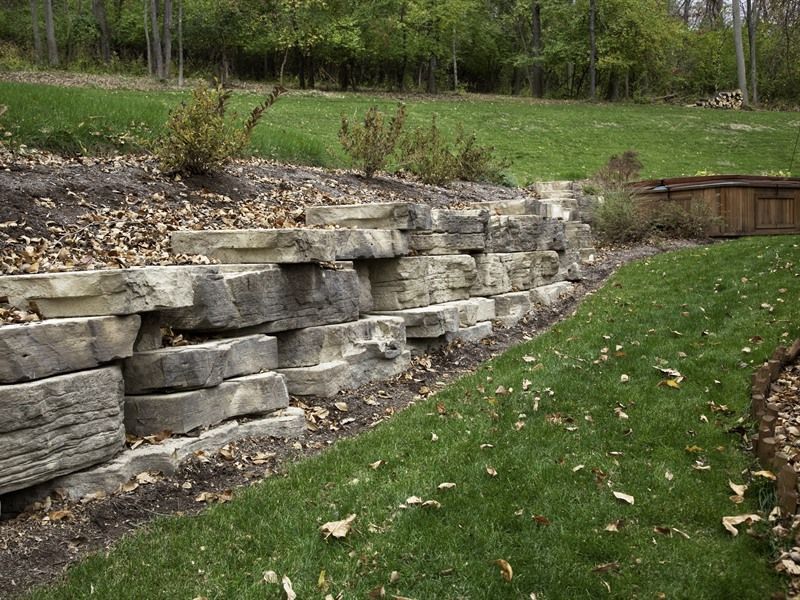 Stone retaining wall on a grassy hillside, with plants at the top.