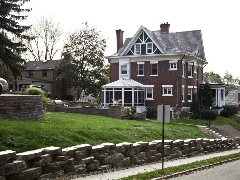 Brick house with porch and gabled roof, on a grassy hill with stone retaining walls.
