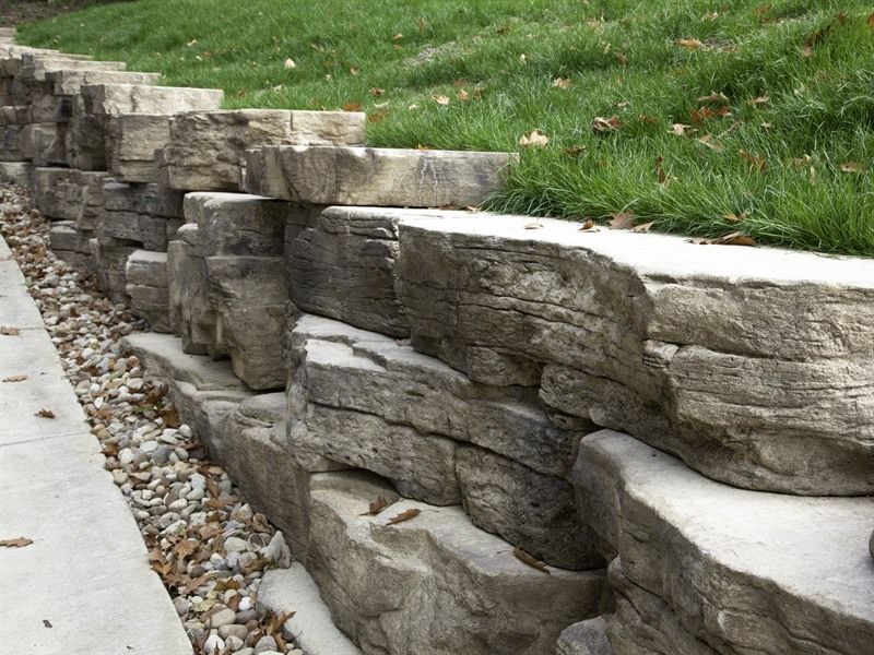 Stone retaining wall along a concrete path, holding back a grassy hill.
