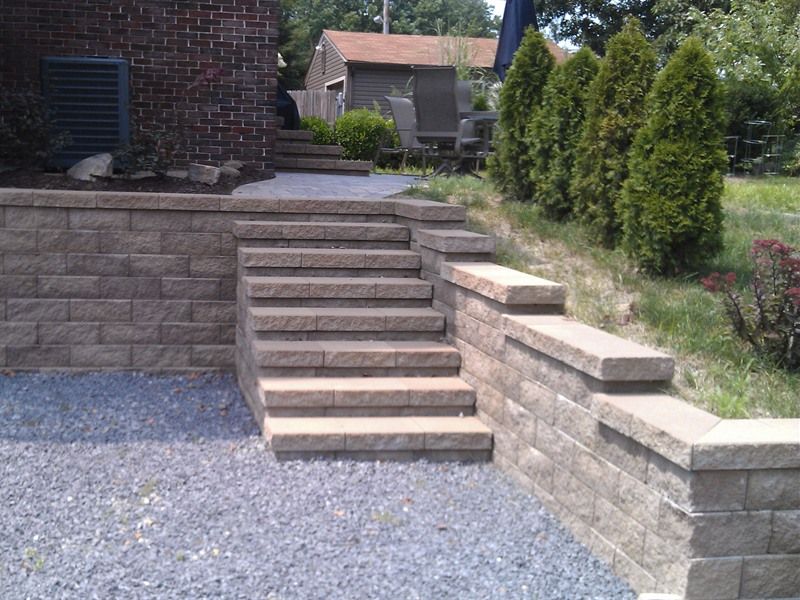 Stone steps and retaining wall leading to a house, gravel ground, green shrubbery.