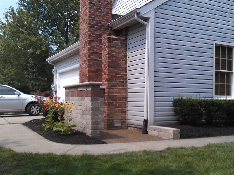 Exterior of a house with a brick chimney and retaining walls, flowers, and a car in the driveway.