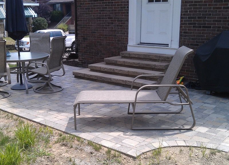 Patio with gray chairs, a table, and steps leading to a white door.