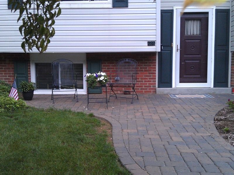 Brick path leading to a home with a brown door, shutters, and two metal chairs.