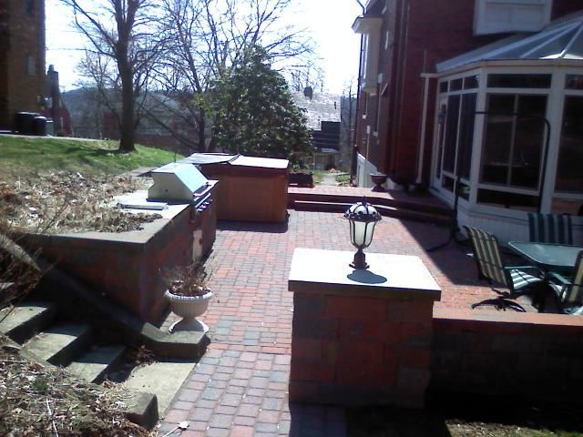 Brick patio with grill, built-in planters, and steps next to a house with a sunroom.