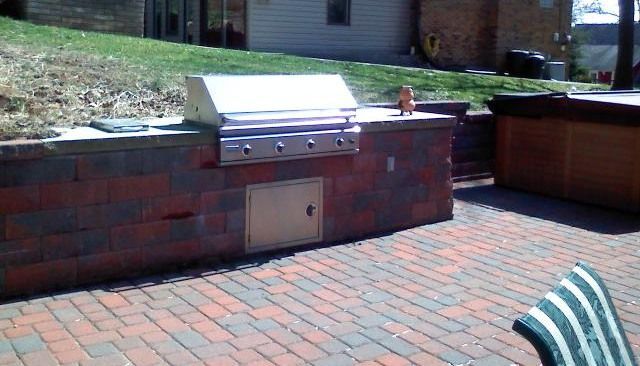 Outdoor brick barbecue island with built-in grill, door, and counter, next to a hot tub.