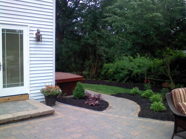 Backyard patio with paved path, small garden beds, and hot tub near a house door.