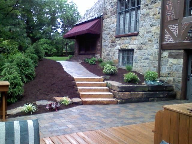 Stone building exterior with brick patio and walkway, landscaping, and steps leading to a covered entrance.