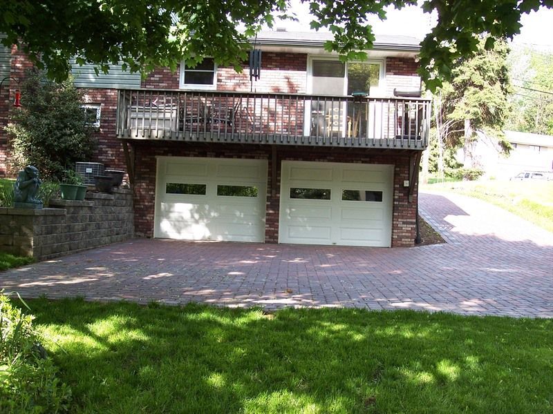Brick house with two-car garage, brick driveway, and a wooden deck above the garage.