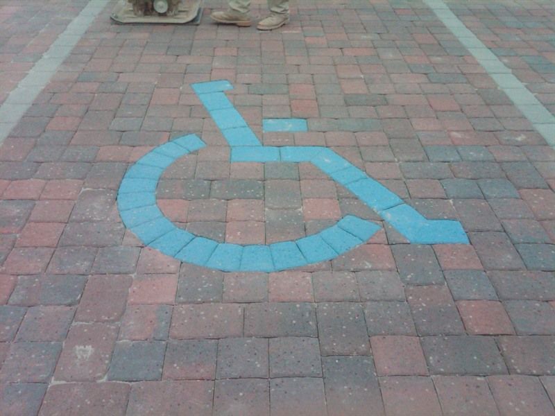 Blue wheelchair symbol painted on brick pavement, designating an accessible parking space.