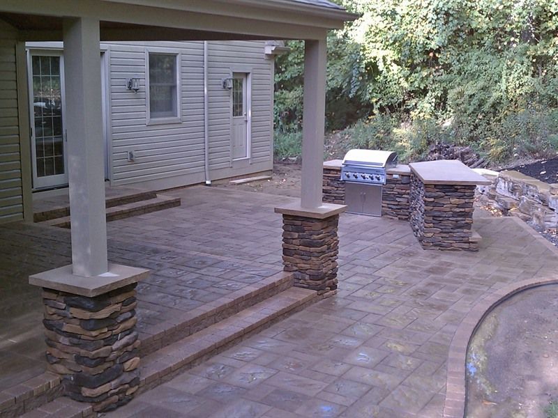 Stone patio with built-in grill and columns under a covered porch.