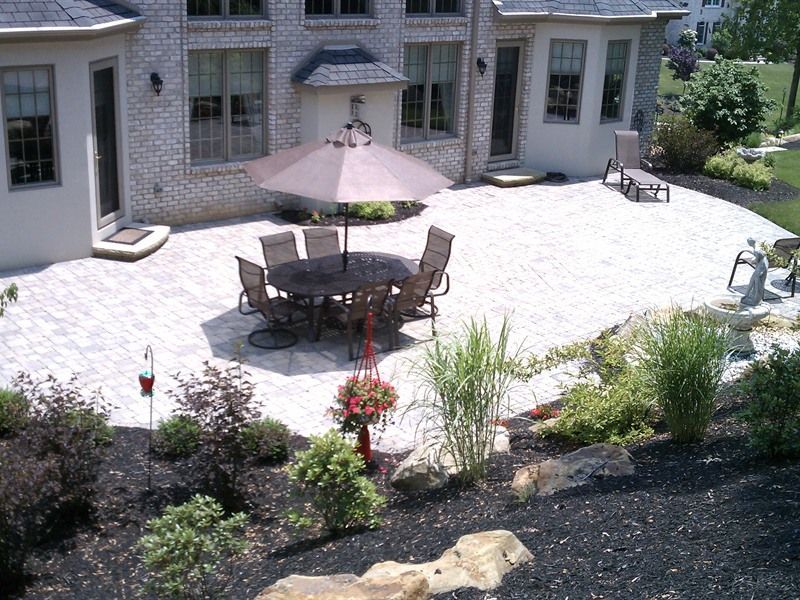 Patio with outdoor dining table and umbrella, surrounded by brick house and landscaping.